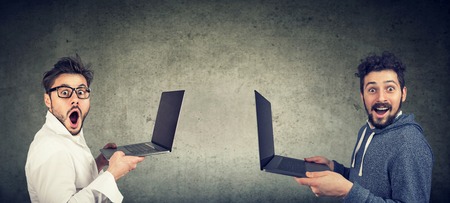 Two surprised funny men with new laptops standing against gray wall background の写真素材