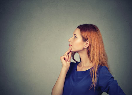 Profile of young redhead woman touching chin and looking up in thoughts and ideasの写真素材