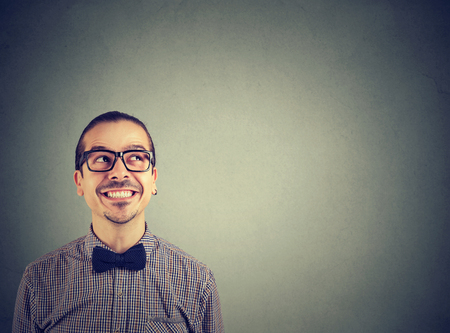 Cheerful stylish man in bow tie and glasses looking up with smile and expression of wondermentの写真素材