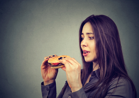 Pretty girl holding delicious cheeseburger and looking totally obsessed with desire to eat it