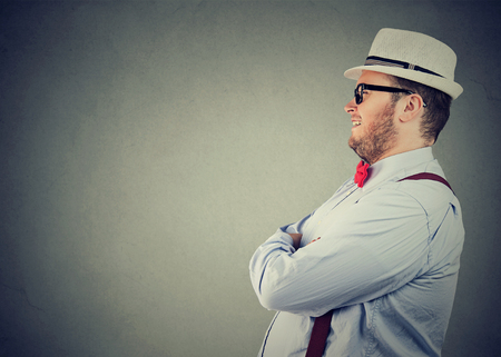 Side view of a chubby happy man in elegant outfit with bow tie and straw hat looking away confidentlyの写真素材