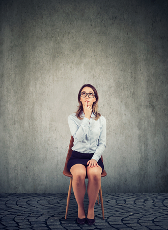 Pensive business woman sitting on chair and contemplating on plan against gray backgroundの写真素材