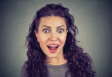 Young casual woman looking amazed while eavesdropping and looking at camera on gray background
