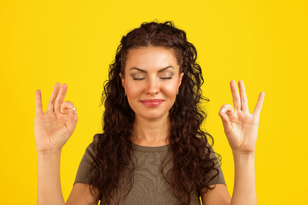 Young woman holding hands in OK signs and keeping eyes closed in relaxation and meditation.の写真素材