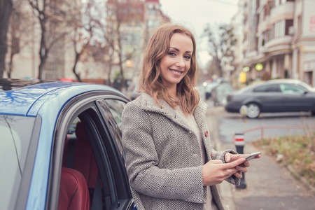 Happy woman using mobile phone standing beside her carの写真素材