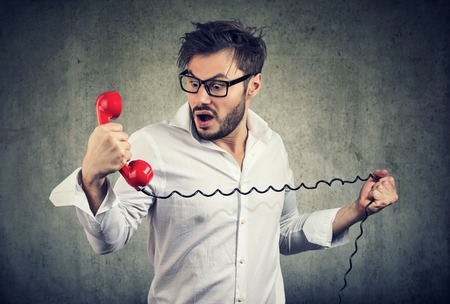 Resentful shocked young man looking in disbelief at telephone handsetの写真素材