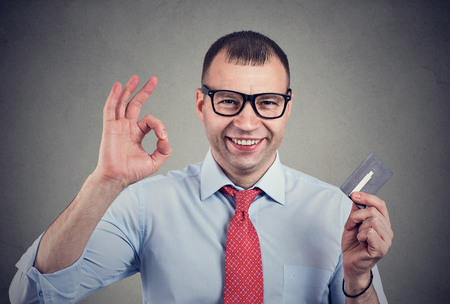 Cheerful happy business man with credit card showing Ok sign on gray backgroundの写真素材