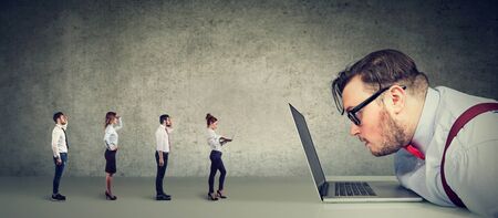 Curious businessman looking at laptop computer analyzing group of businesspeople in miniature applying online for a jobの写真素材