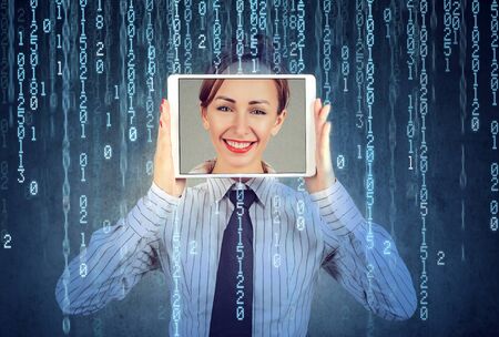 Happy woman holding tablet with her face displayed on a screen isolated on binary code background の写真素材