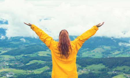Happy young woman standing with arms raised at mountain peakの写真素材