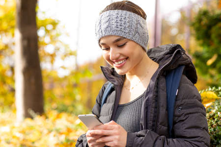 Portrait of a young happy woman reading sms on cellphone outdoors in park