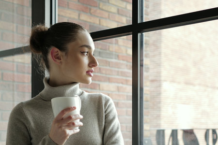 woman with a cup of coffee looking in the windowの写真素材