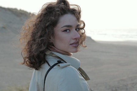 Portrait of a young woman standing on a beach looking at camera. Smiling, happy mixed race girl in casual outfit with wind in her hair.の写真素材
