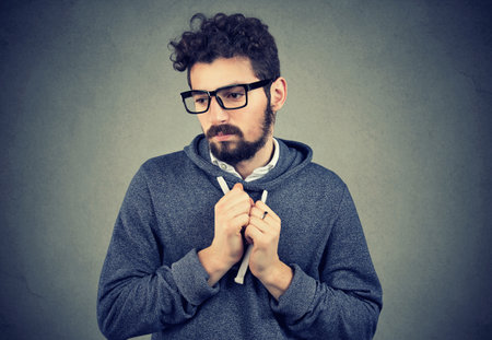 Lack of confidence. Shy anxious young man feels awkward isolated on grey wall background.の写真素材