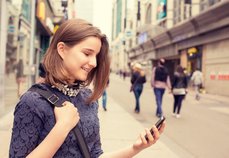 Portrait happy girl walking and texting on the smart phone in the street wearing a dress in autumn. Urban city background. Attractive woman using mobile phoneの写真素材