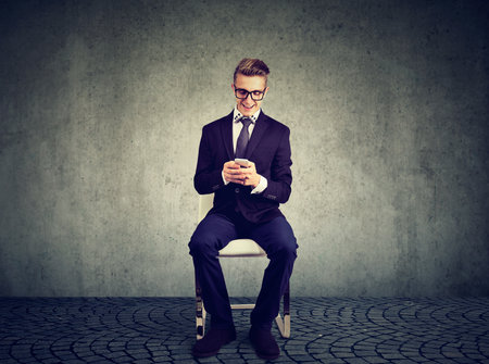 Smiling businessman sitting on a chair uses his mobile phoneの写真素材