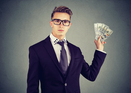 Serious business man showing dollar banknotes isolated on gray wall backgroundの写真素材