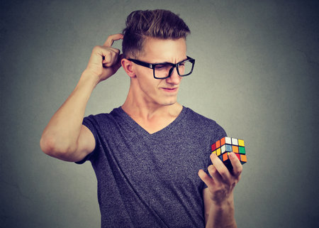 Young man holding Rubikâs cube thinking, focused on a task.の写真素材