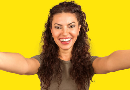 Portrait of a happy beautiful woman taking a selfie isolated on yellow backgroundの写真素材
