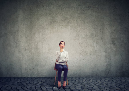 Business woman sitting on a chair, thinking, looking upの写真素材