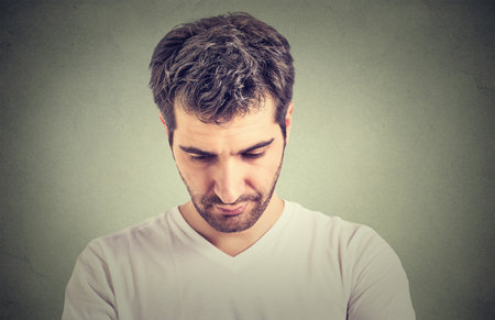 Sad lonely young man looking down has no energy motivation in life depressed isolated on gray wall backgroundの写真素材