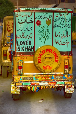 A three-wheeler taxi in Pakistan, also known as samosa, tempo, tuk-tuk, trishaw, autorick. Painted with flowers and urdu slogansのeditorial素材