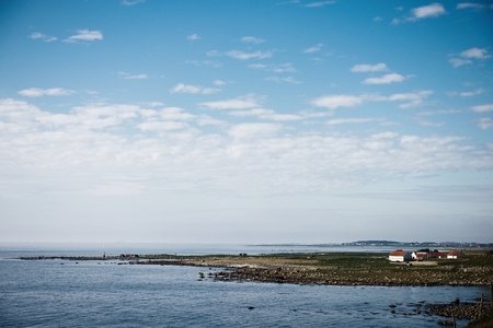 Wooden cottage, sauna on shore. Tiny house near the water. Rocky small island, islet in water. Buildings surrounded by green treesの写真素材