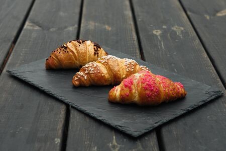 freshly baked croissants on wooden cutting board, top view, black stone