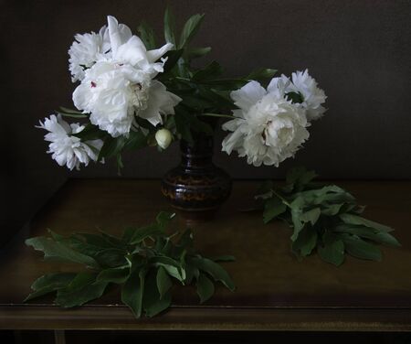 Still life with huge bunch of white, red and pink peonies, red apple and open book on painting backgroundの写真素材