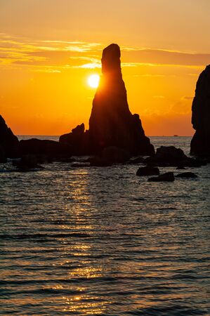 Rocks and sunrise sticking out of the seaの写真素材
