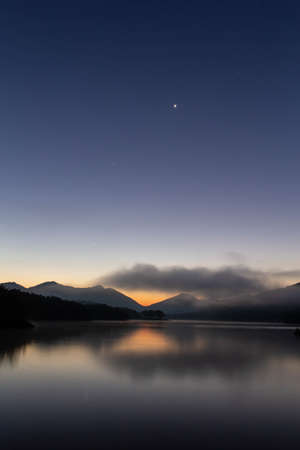 A beautiful lake at dawn with clouds and stars