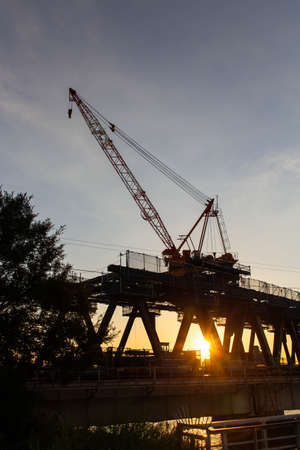 A steel bridge under construction, a sunset and a huge craneの写真素材