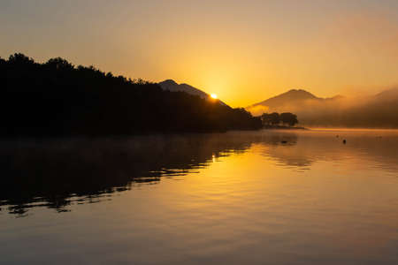 Sun and lake rising from the orange morning skyの写真素材