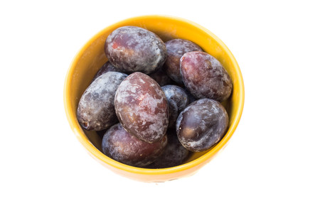 blue purple plums in orange bowl isolated on white backgroundの写真素材