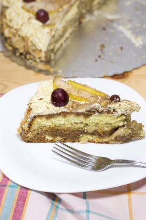 slice of delicious homemade cake with coffee cream decorated by red grape and pears on white plate  on wood tableの写真素材