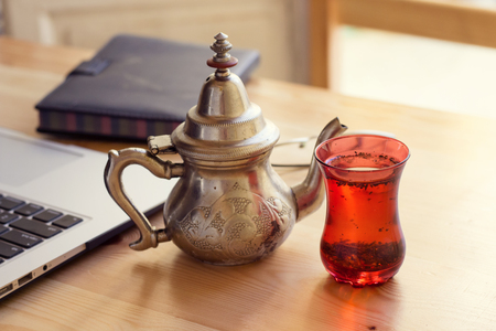 office desk gray laptop silver arabic tea pot and notebook red cupの写真素材