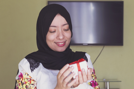 beautiful muslim woman with cheerful smile hold a white gift box with red ribbonの写真素材