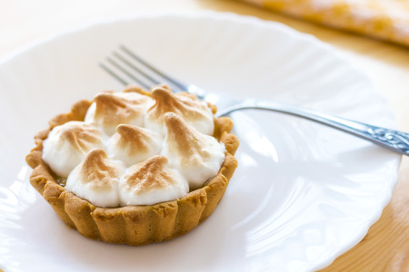 home made tartlet with meringue and lemon cream on a white plate,silver forkの写真素材