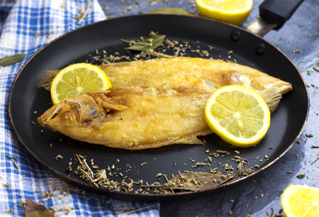 delicious ready sole fish on black pan and decorated with lemon and herbsの写真素材