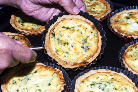 Baked homemade quiche pie in mini metal forms and woman hand holding one pie