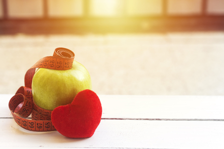 green apple with tape measure and red heart cotton  on white wood table,Concept for diet, healthcare, nutrition or medical insuranceの写真素材