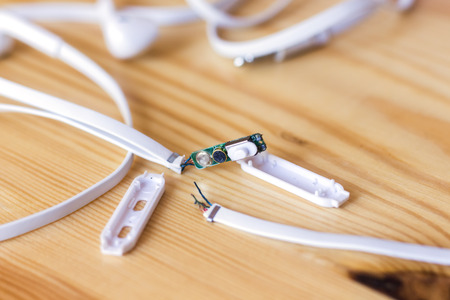Broken white audio headphones cable lying on wooden surfaceの写真素材
