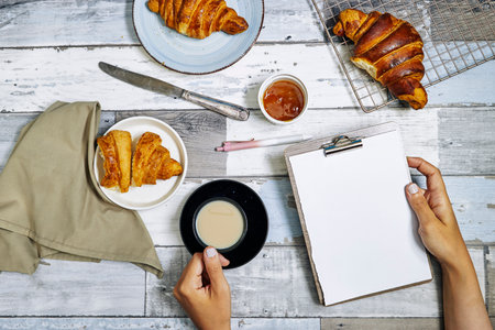 Fresh sweet croissants with orange jam for breakfast. Continental breakfast on wooden table, hand hold empty clipboard. Top view. Flat layの写真素材