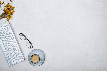 top view of desktop, close up of keyboard, cup of coffee and gypsophila flowers with eyeglasses on...