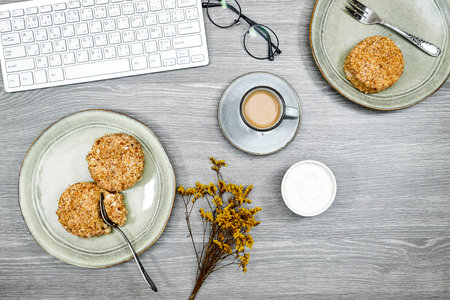 top view of desktop, homemade cake with cup of milk coffee, eyeglasses and gypsophila and keyboardの写真素材