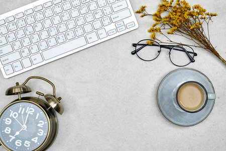 top view of desktop, alarm clock with cup of milk coffee, eyeglasses and gypsophila and keyboard