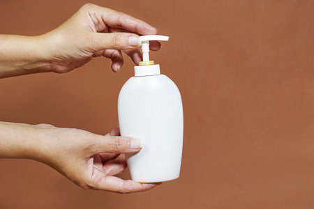 Female hand holding cream bottle of lotion isolated. Girl give tube cosmetic products on brown backgroundの写真素材