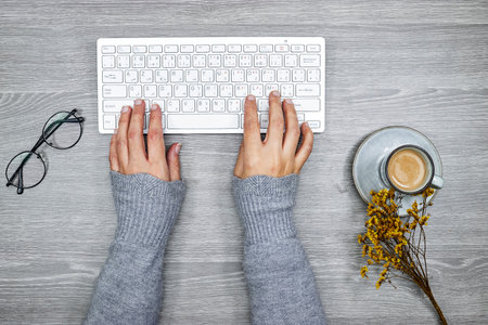 top view of desktop, close up of female hands typing on keyboard, cup of coffee and gypsophila...