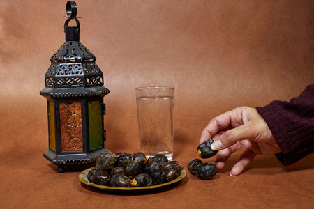 ramadan iftar concept, dates fruits with glass water and lantern and woman hand holding one piece