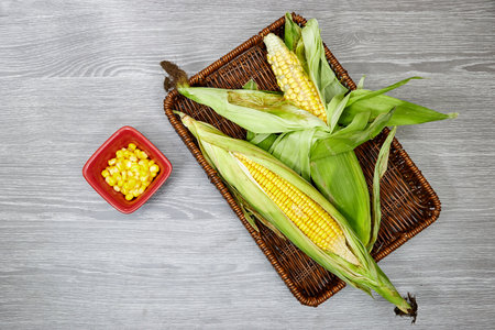 Fresh corn cob in esparto halfah basket and bowl on wood table